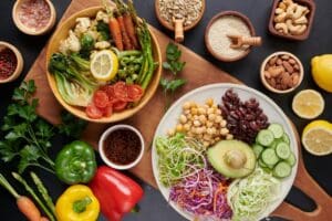 Un assortiment coloré de légumes frais, de légumineuses et de graines disposés dans des assiettes et des bols met en valeur des ingrédients vibrants parfaits pour les recettes végétariennes, notamment l'avocat, les pois chiches, les haricots rouges, le concombre, le chou, les poivrons, les noix et les moitiés de citron.