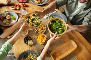Un groupe de personnes partage des bols de salade autour d'une table en bois garnie d'assiettes de nourriture, de nachos, d'olives et de boissons, créant ainsi une scène de repas chaleureuse et invitante, propice aux bonnes conversations.